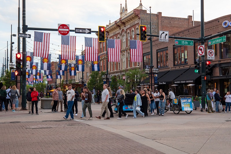 Larimer Square in downtown Denver, Colorado, with historic brick buildings, American flags, and pedestrians crossing the street.